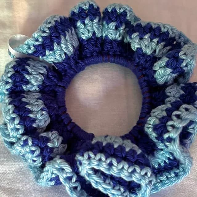 Chouchou au crochet bleu marine et bleu ciel, posé sur un tissu clair.