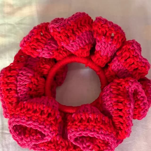 Chouchou au crochet rouge et rose, posé sur un tissu clair.