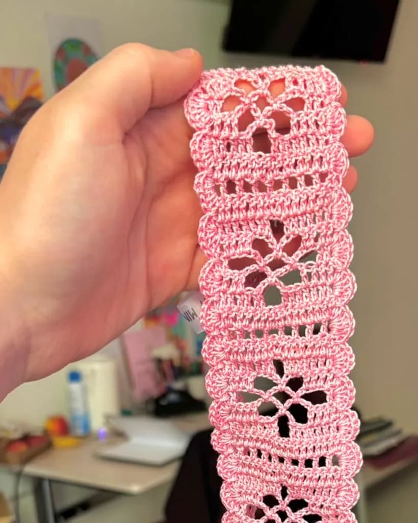 Manon tient un bandeau au crochet rose à motifs de dentelle.